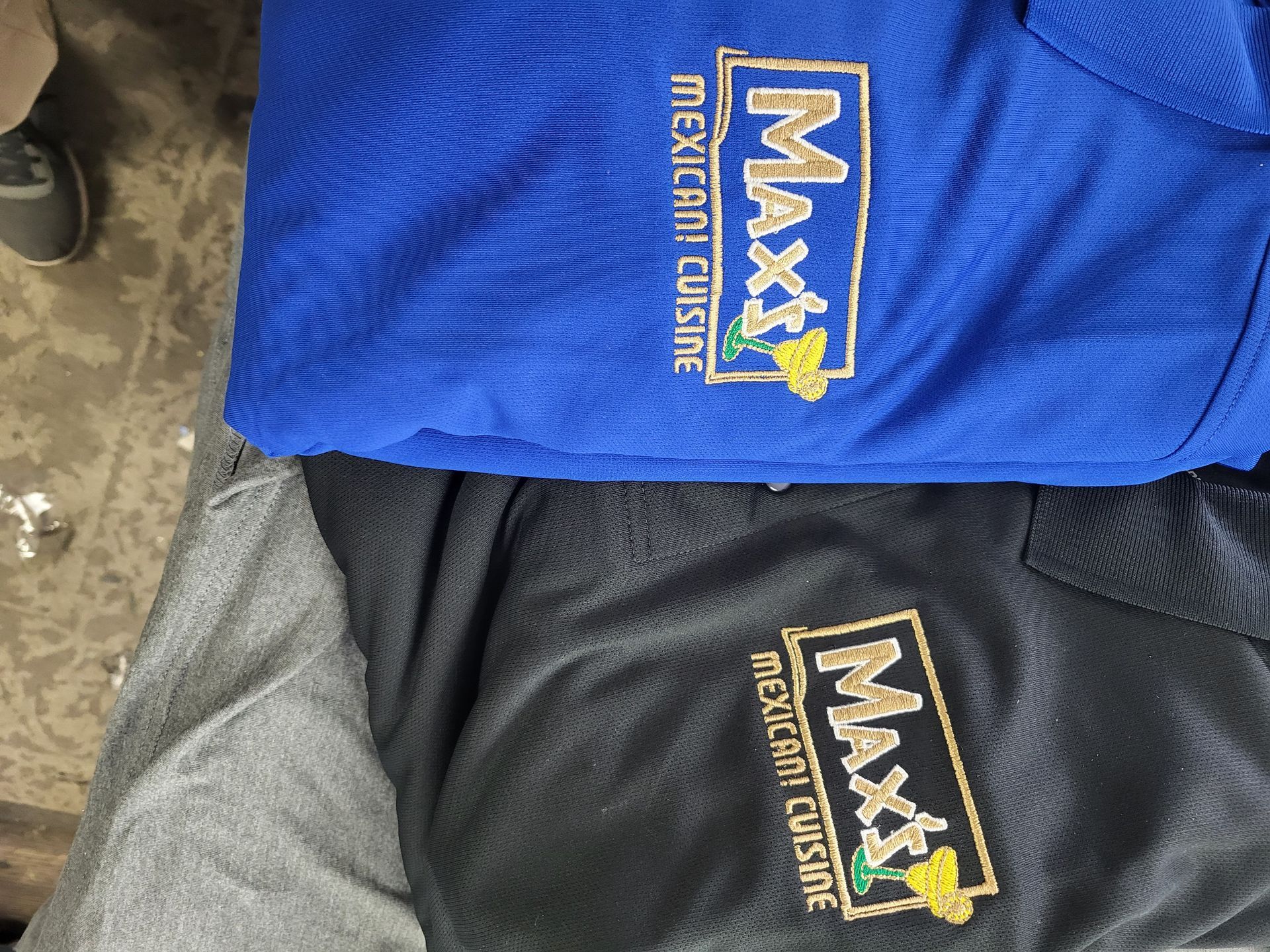 A blue shirt and a black shirt, each embroidered with a logo for 