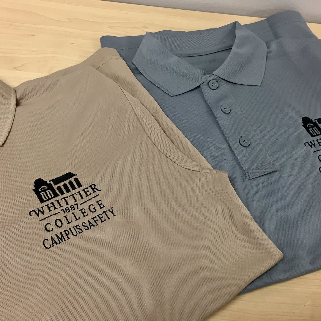 Two polo shirts on a wooden surface, one tan and one blue, both embroidered with the Whittier College Campus Safety logo.