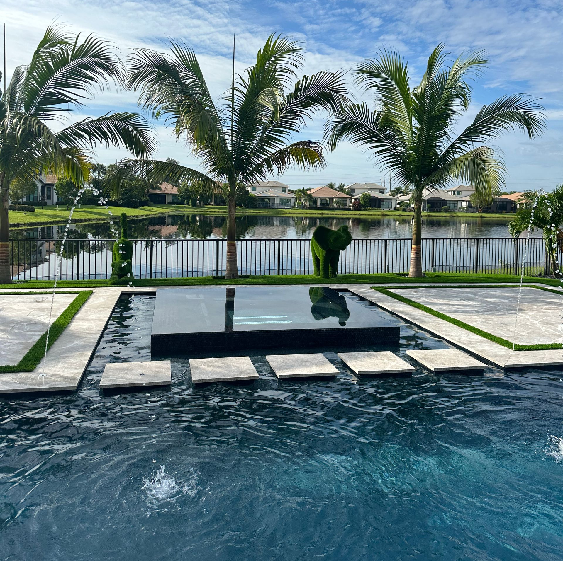 Lush South Florida backyard with tropical plants, palms, water feature, and artificial turf designed by The Time Is Now Design and Build.