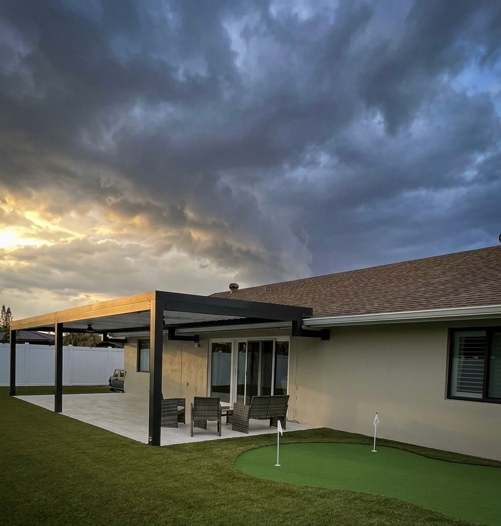 A view of a modern patio featuring a black louvered pergola with a cloudy sky