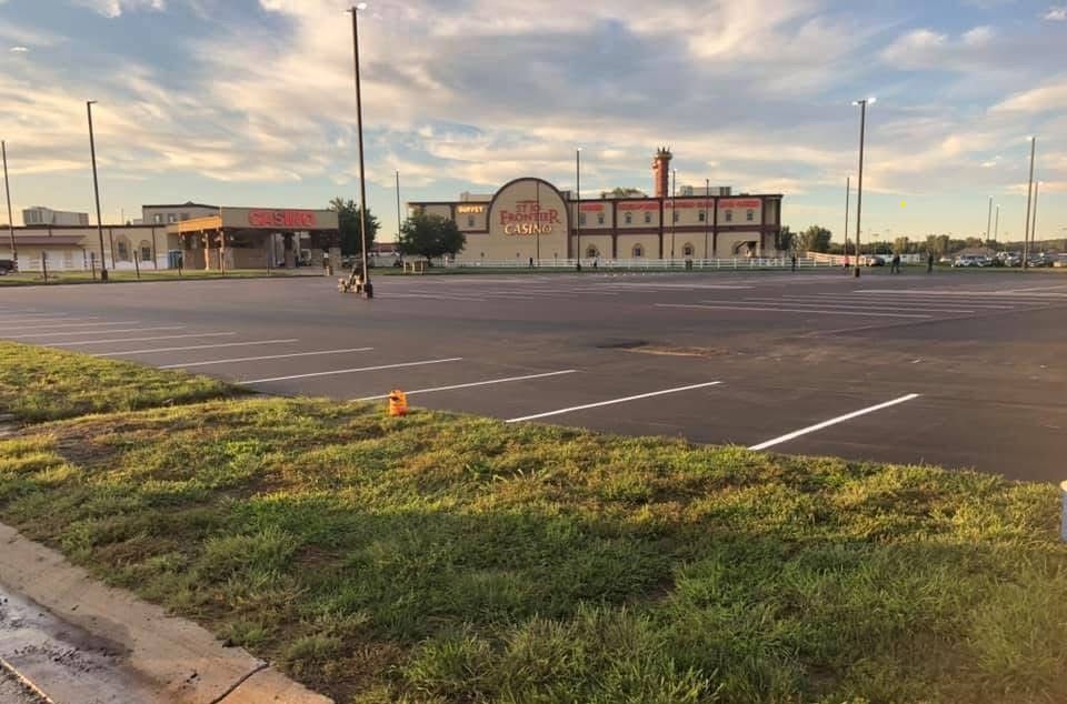Empty parking lot in front of a large brick building with a red sign and a smokestack, under a cloudy sky.