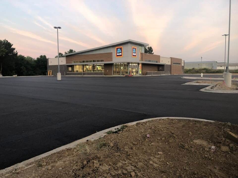 Exterior view of an Aldi grocery store with a freshly paved, empty parking lot under a dusk sky.