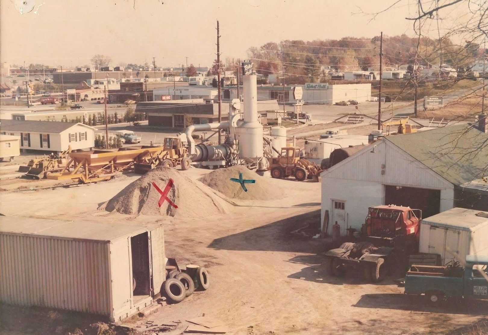 An aerial view of a construction site with buildings, heavy machinery, and piles of gravel in an industrial area.