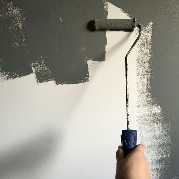 Hand painting a gray wall with a paint roller, covering white paint.
