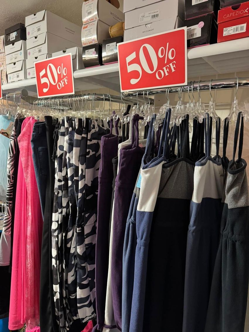 Clothing rack with 50% off sale signs, featuring various colored dresses and pants in a store.