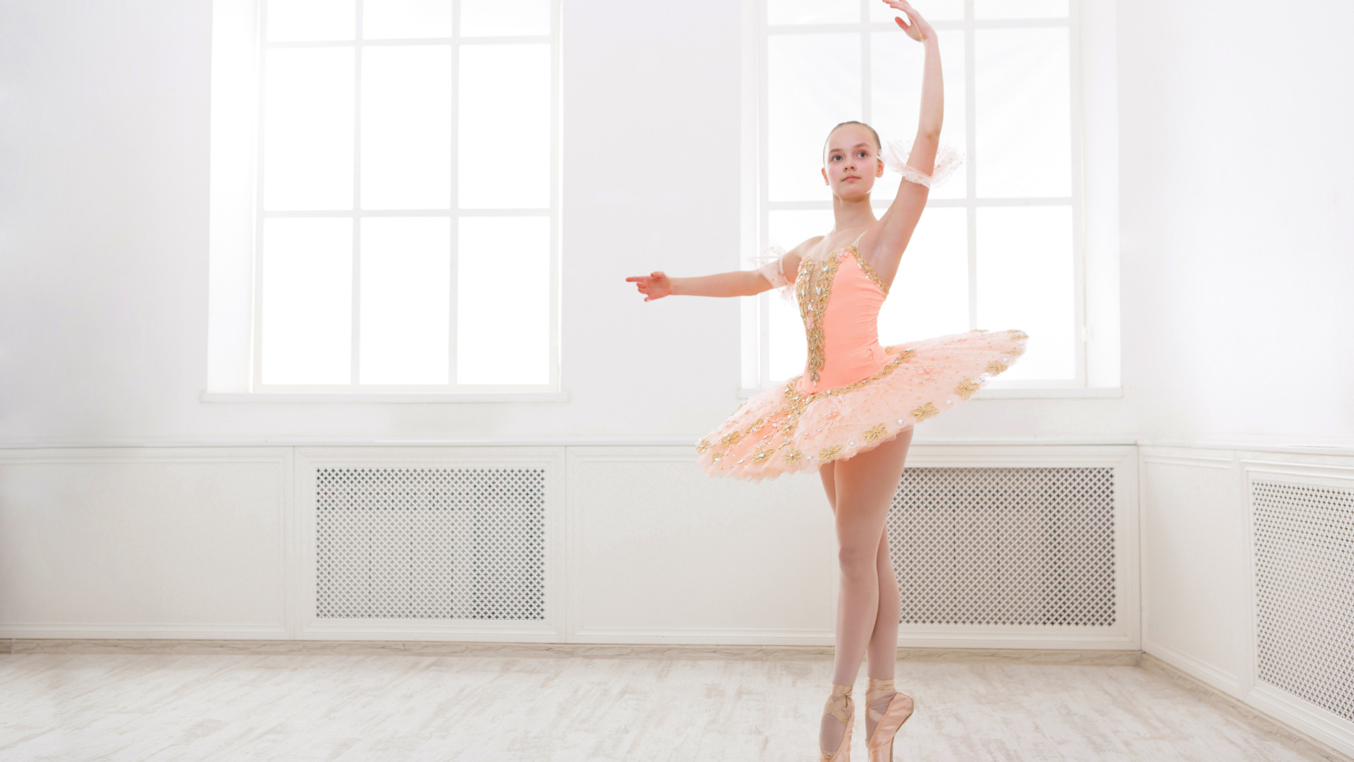 Ballerina in pink tutu and pointe shoes, performing a graceful pose in a bright studio.