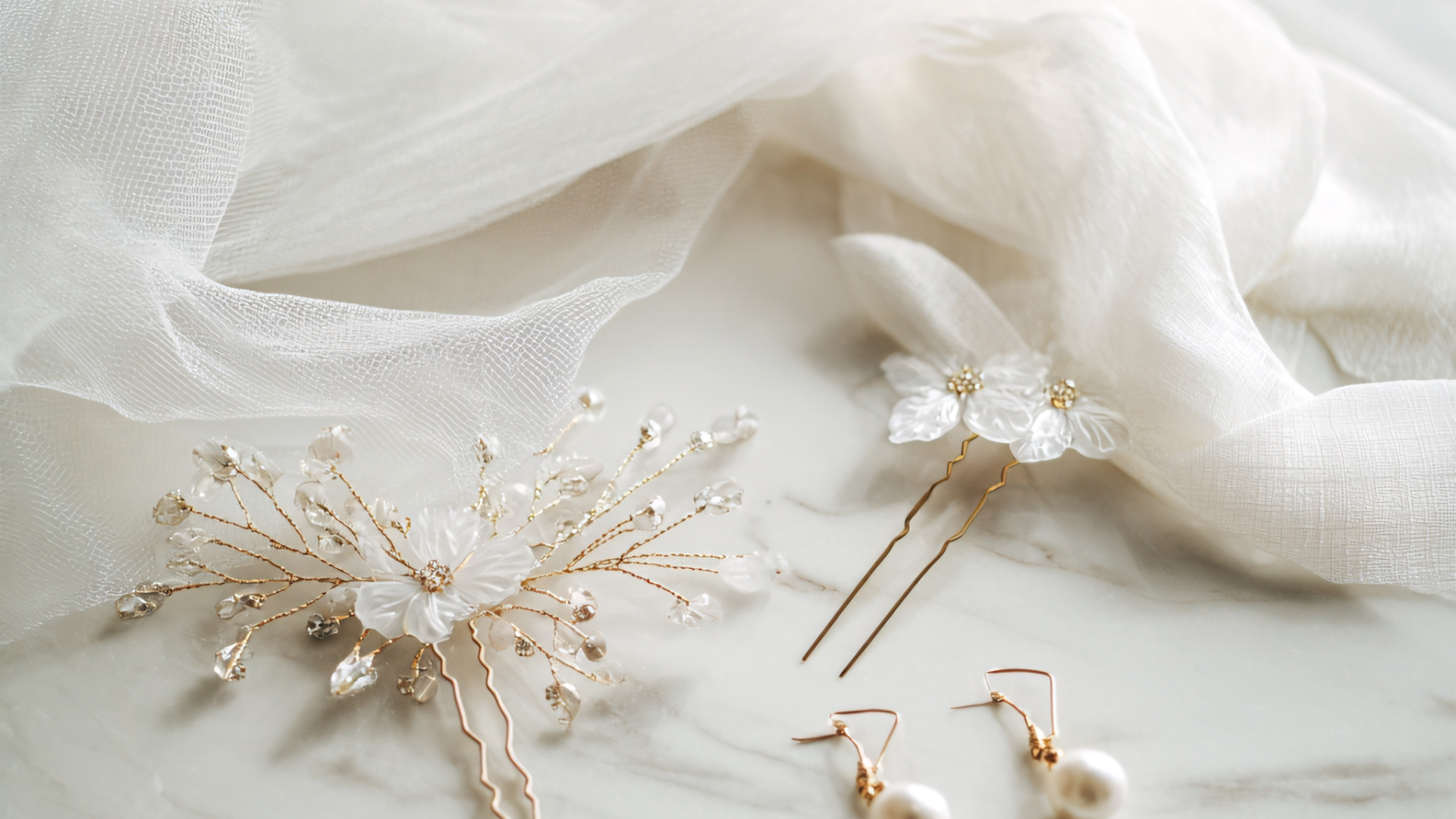 Elegant bridal accessories: flower hairpins, earrings, and a sprig, on sheer white fabric.
