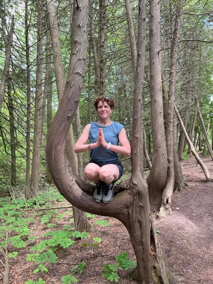 A woman is sitting on a tree branch in the woods.