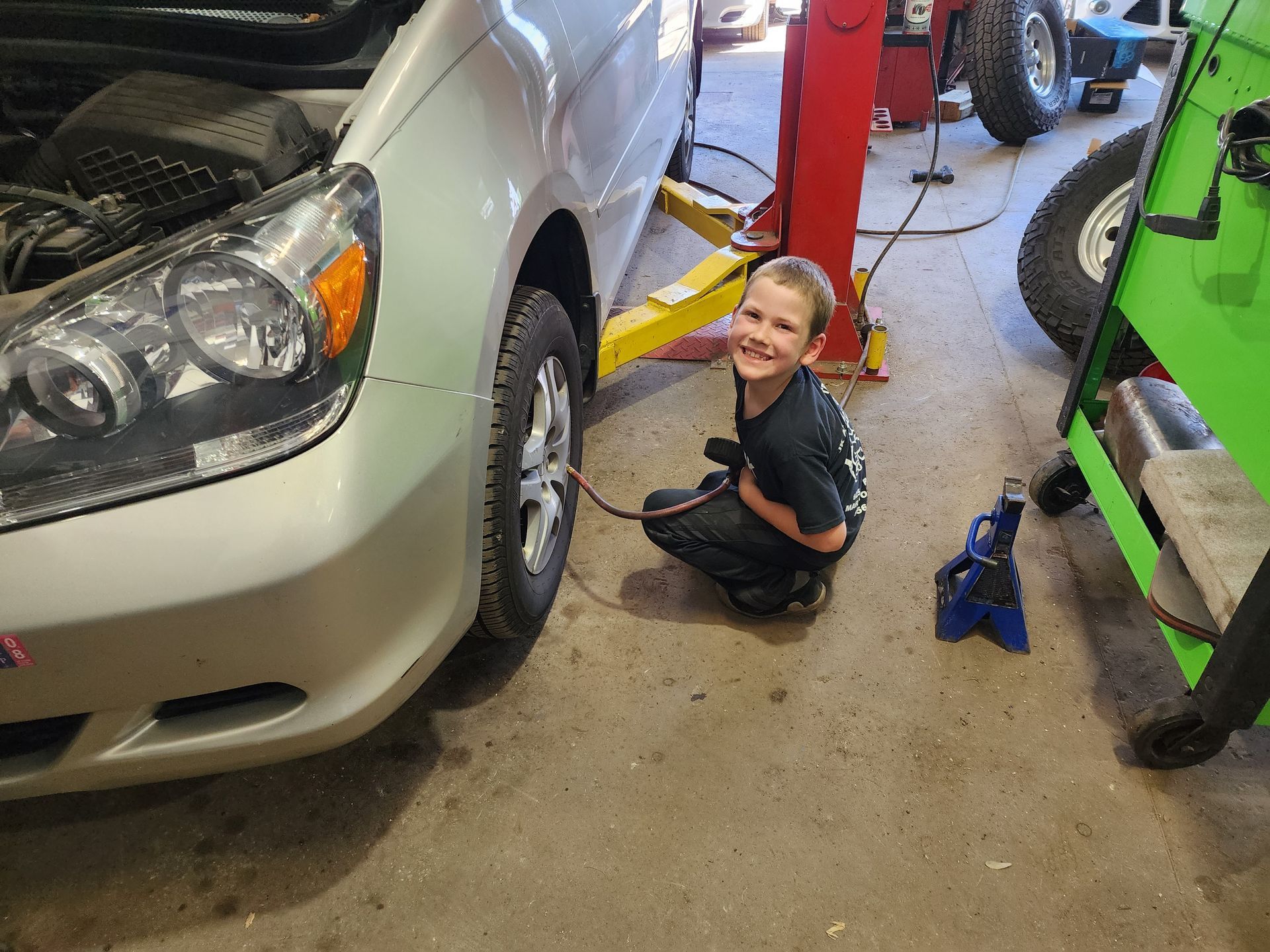 Smiling child in a garage beside a silver car | JK Auto And Truck Repair