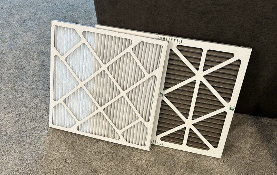 A clean white air filter next to a dirty brown air filter.