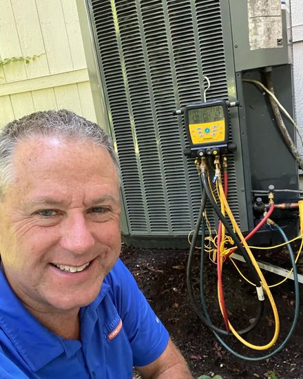 Smiling man checks AC unit with gauge set; outdoors.