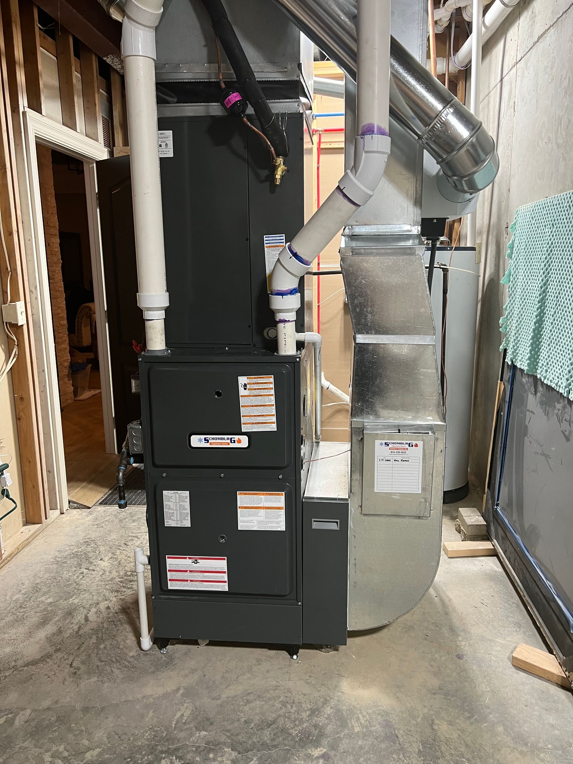 A gray furnace with white pipes and ductwork in a basement setting.