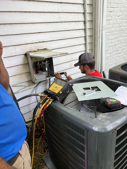 HVAC technician working on an air conditioner outside a white building, using gauges.