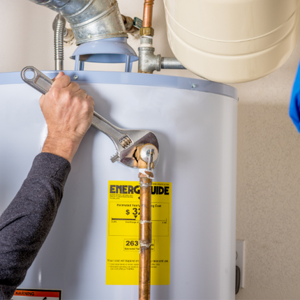 Person using a wrench to work on a water heater near a copper pipe and a yellow energy guide sticker.