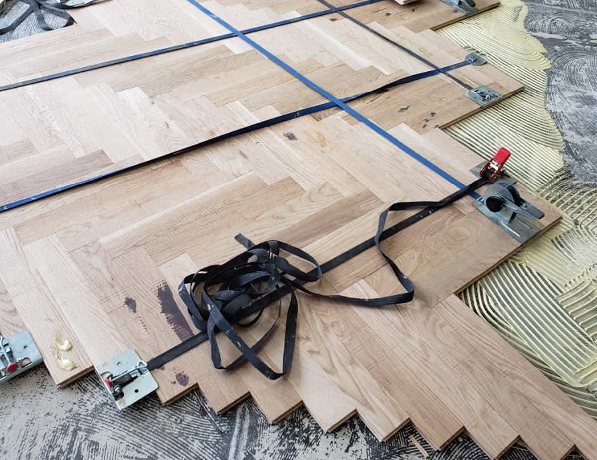 Herringbone wood floor installation with straps and clamps securing the pattern.
