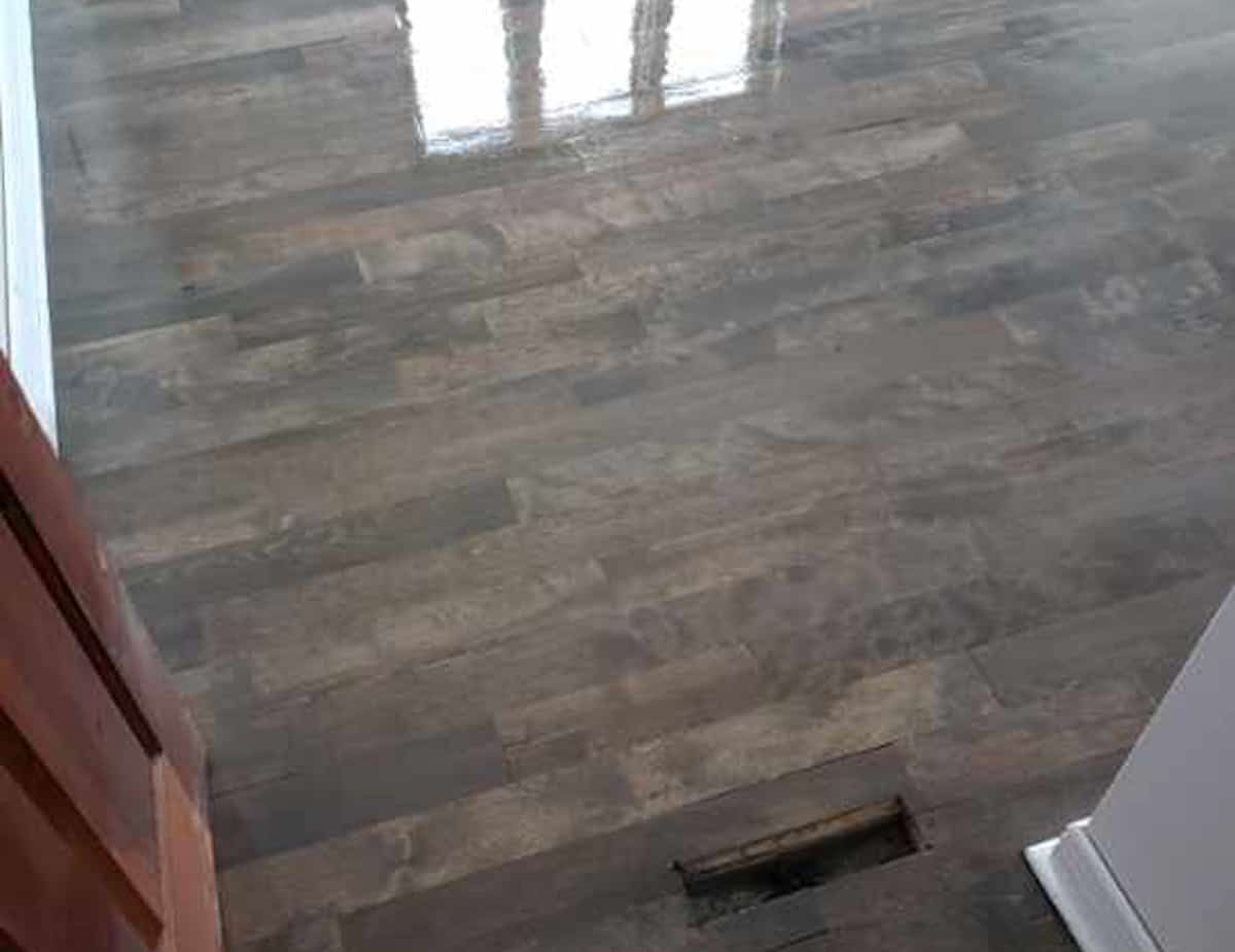 Wood-look floor with dark brown and grey tones, reflecting light. Air vent visible.