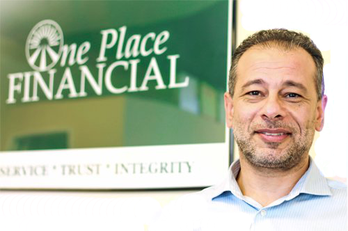 A man stands in front of a sign that says one place financial