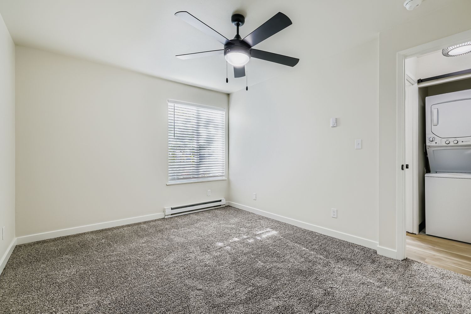 Photo of a large, carpeted bedroom with a ceiling fan and the washer/dryer area in the background