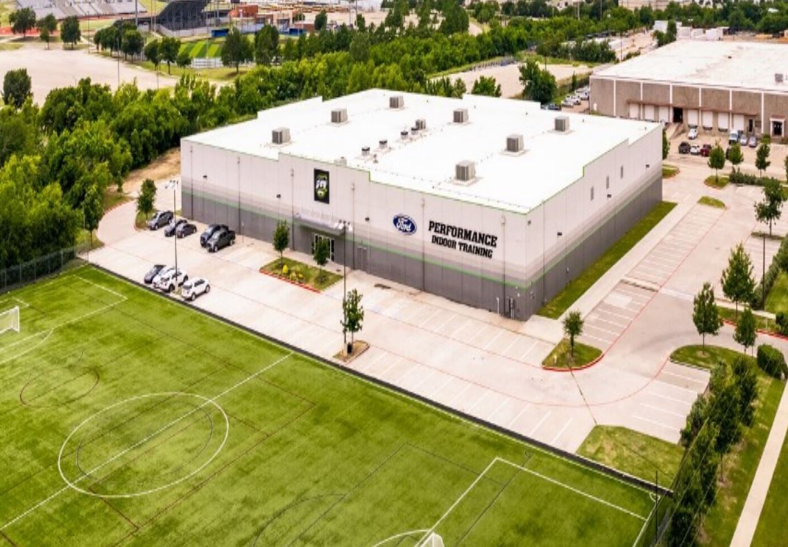 An aerial view of a large building with a soccer field in front of it.