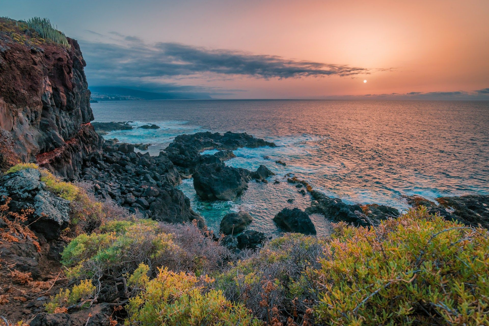 A sunset over the ocean with a cliff in the foreground.