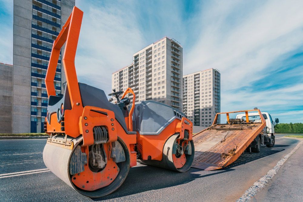 An Orange Road Roller Is Next to A Tow Truck — Watto's Earthmoving & Machinery Hire in Atherton, QLD