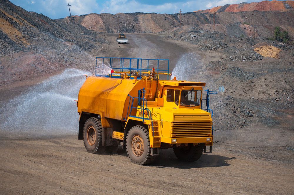 A Yellow Dump Truck Is Spraying Water in A Quarry — Watto's Earthmoving & Machinery Hire in Atherton, QLD
