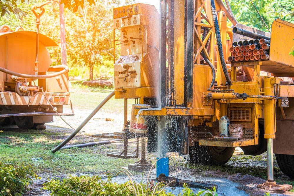 A Yellow Truck Is Drilling a Hole in The Ground — Watto's Earthmoving & Machinery Hire in Atherton, QLD