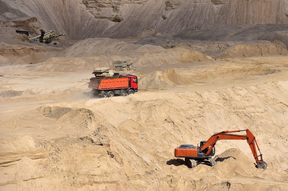 A Dump Truck Is Driving Down a Dirt Road Next to An Excavator — Watto's Earthmoving & Machinery Hire in Atherton, QLD