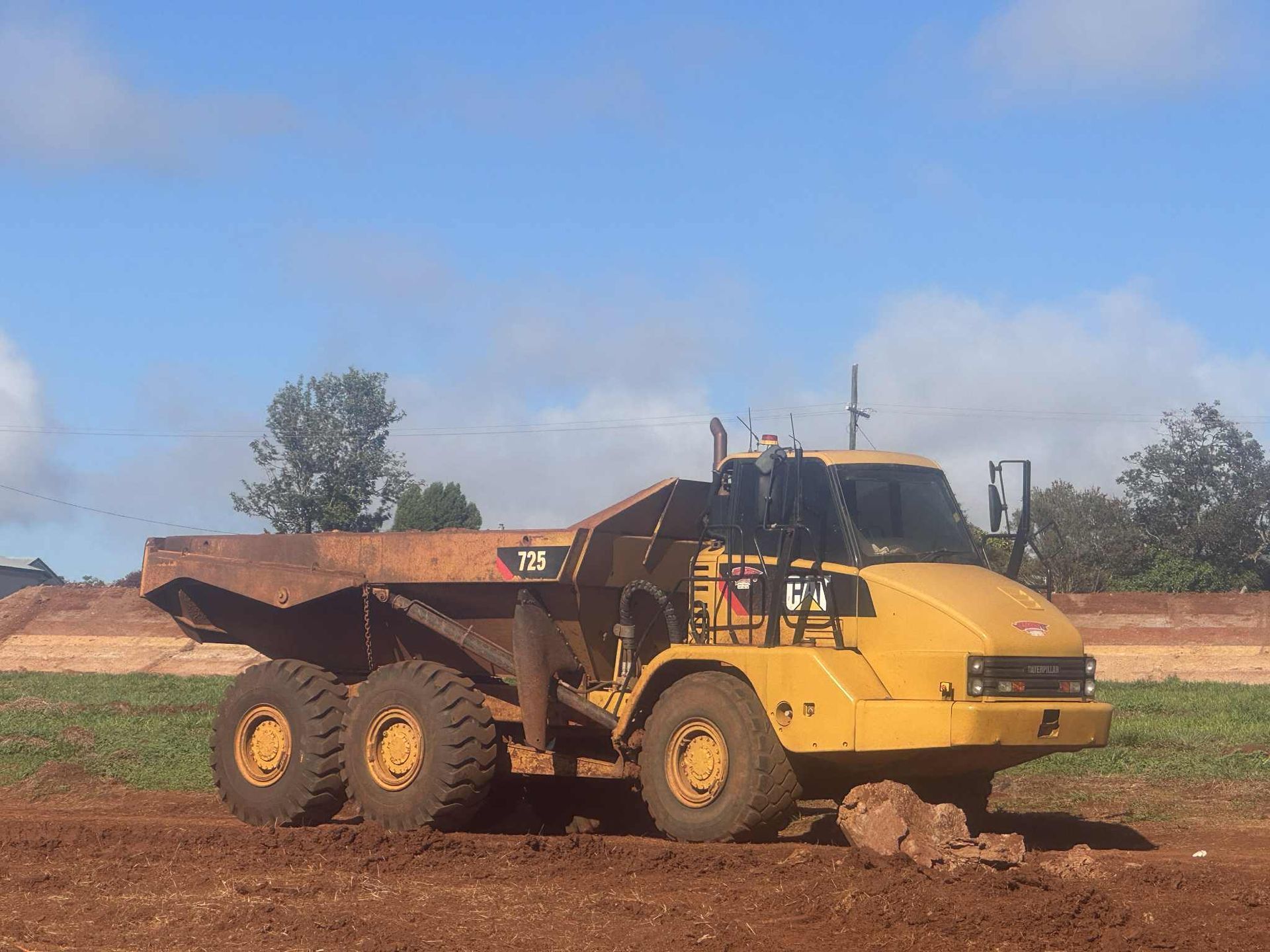 A Man Is Driving a Bulldozer in A Dirt Field — Watto's Earthmoving & Machinery Hire in Atherton, QLD