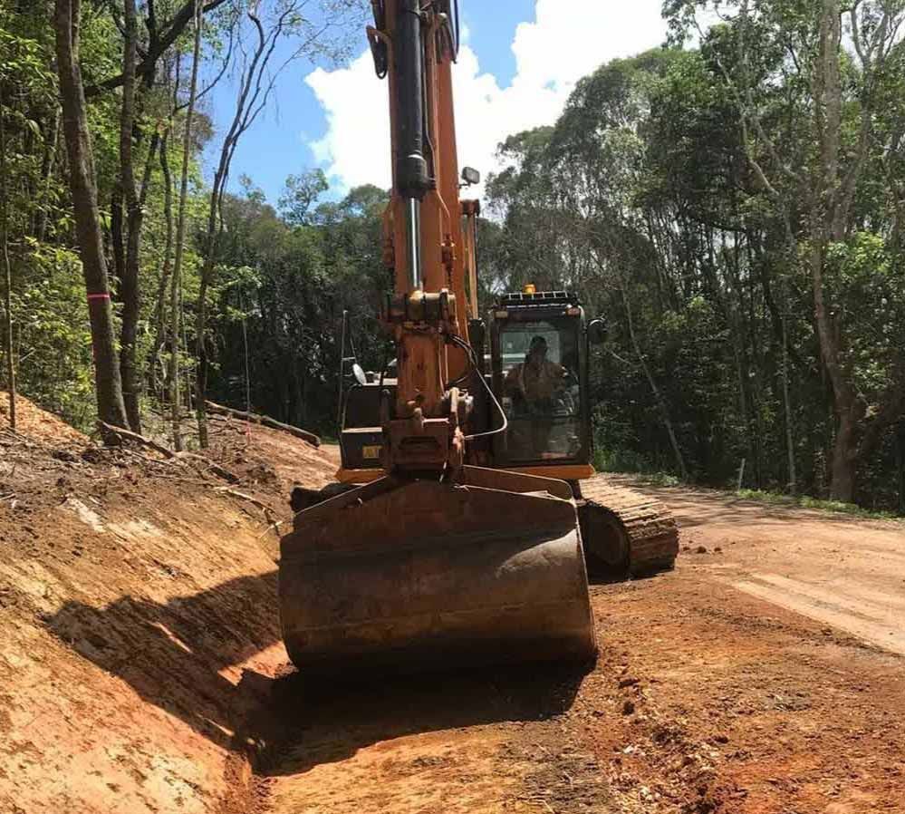 A Bulldozer Is Driving Down a Dirt Road in The Woods — Watto's Earthmoving & Machinery Hire in Atherton, QLD
