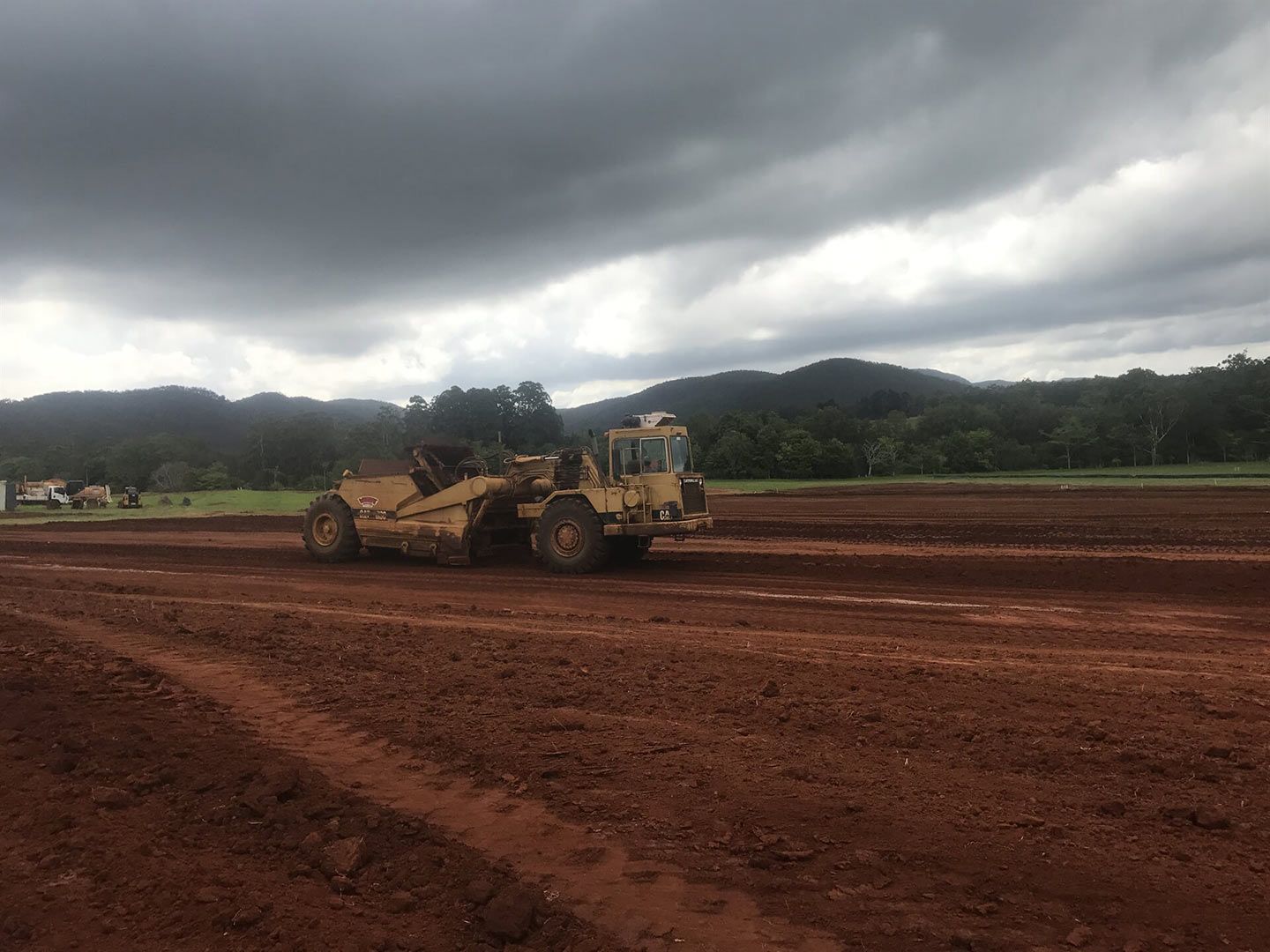 A Bulldozer Is Moving Dirt in A Field on A Cloudy Day — Watto's Earthmoving & Machinery Hire in Atherton, QLD
