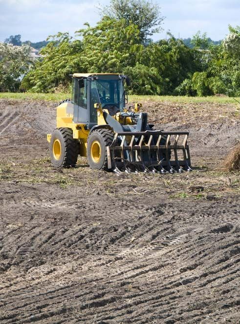 A Yellow Tractor Is Driving Through a Dirt Field — Watto's Earthmoving & Machinery Hire in Atherton, QLD