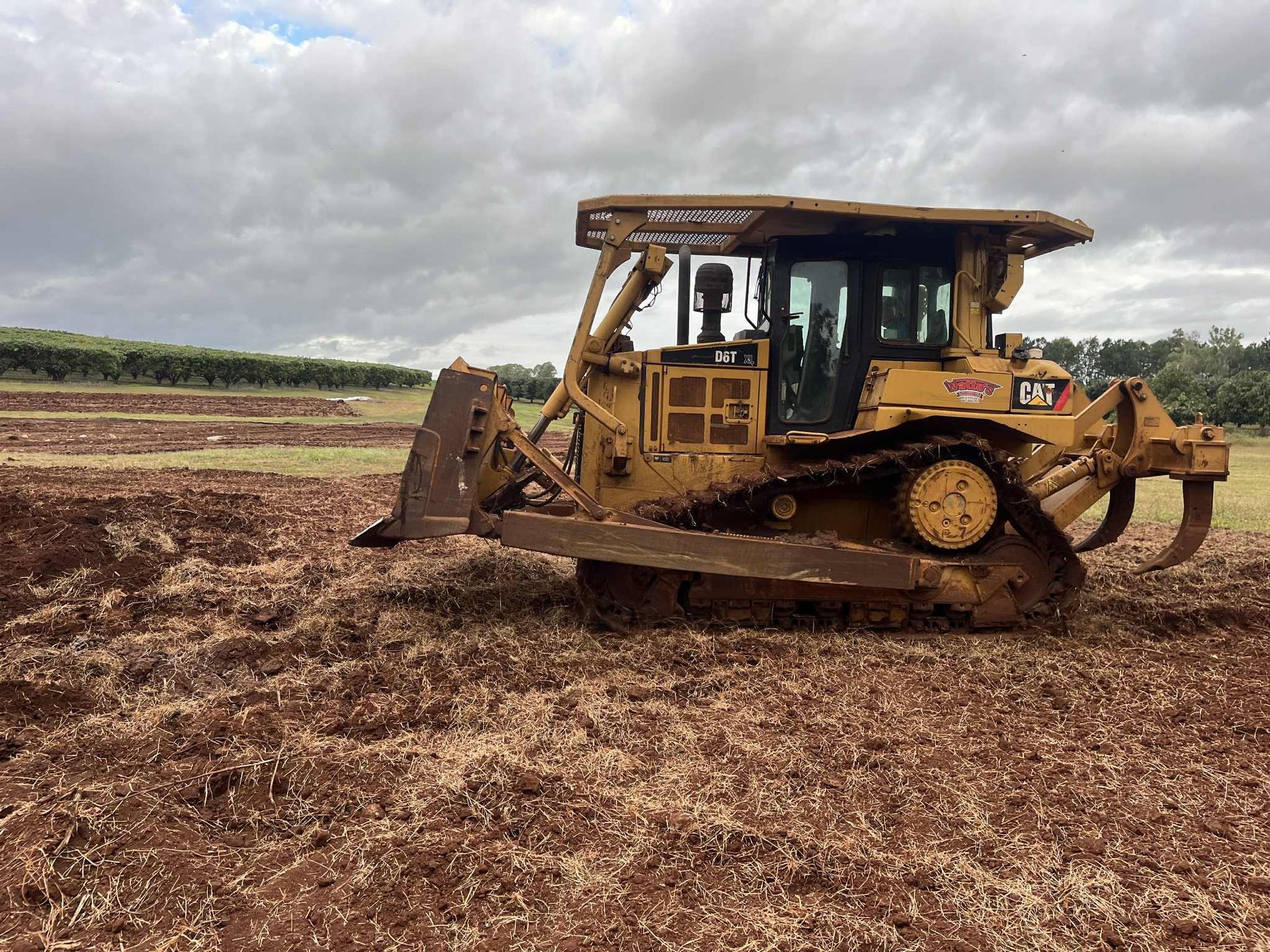A Man Is Driving a Bulldozer on A Dirt Road — Watto's Earthmoving & Machinery Hire in Atherton, QLD