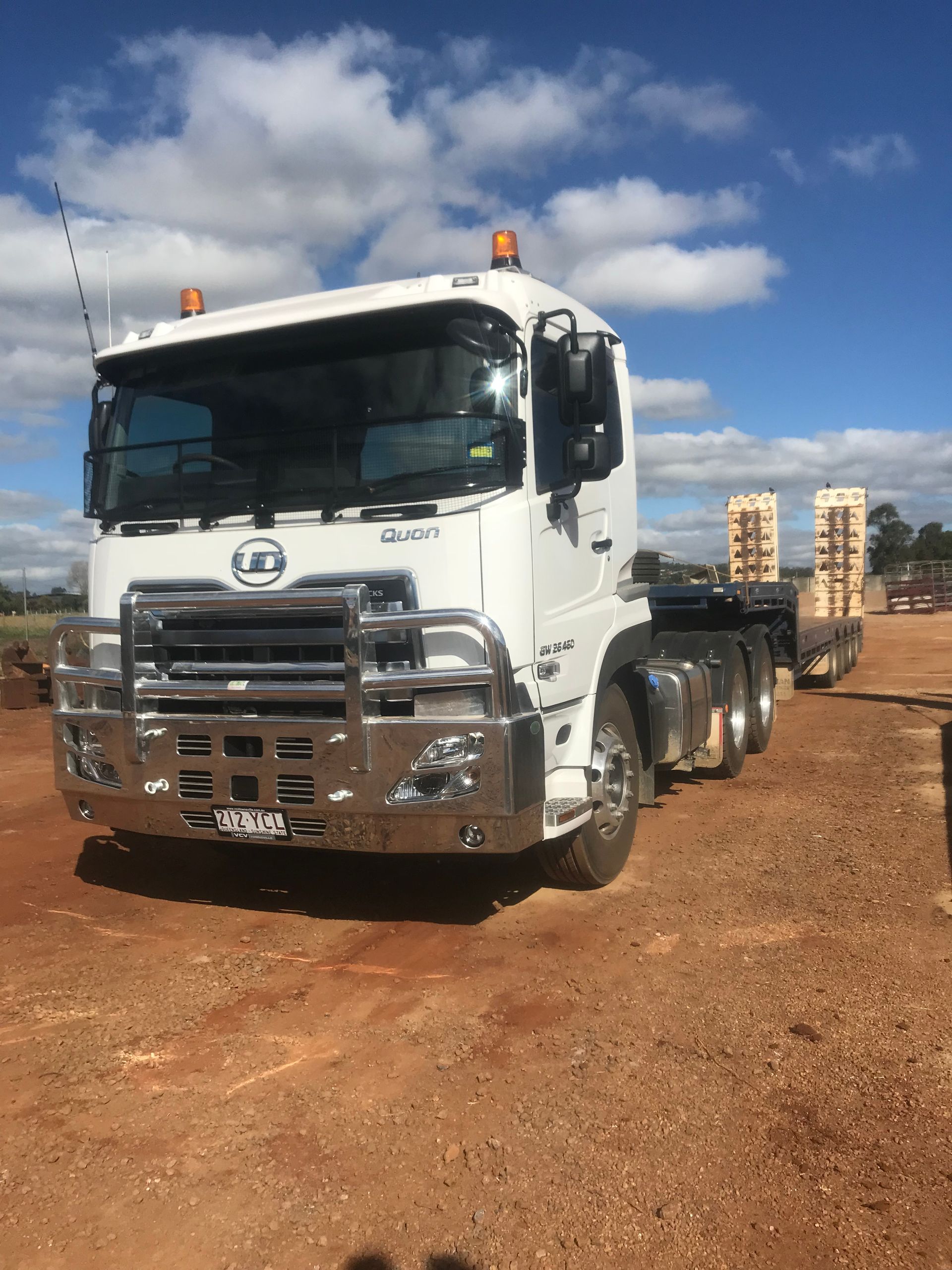 A Yellow Truck Is Spraying Water on A Dirt Road — Watto's Earthmoving & Machinery Hire in Mareeba, QLD