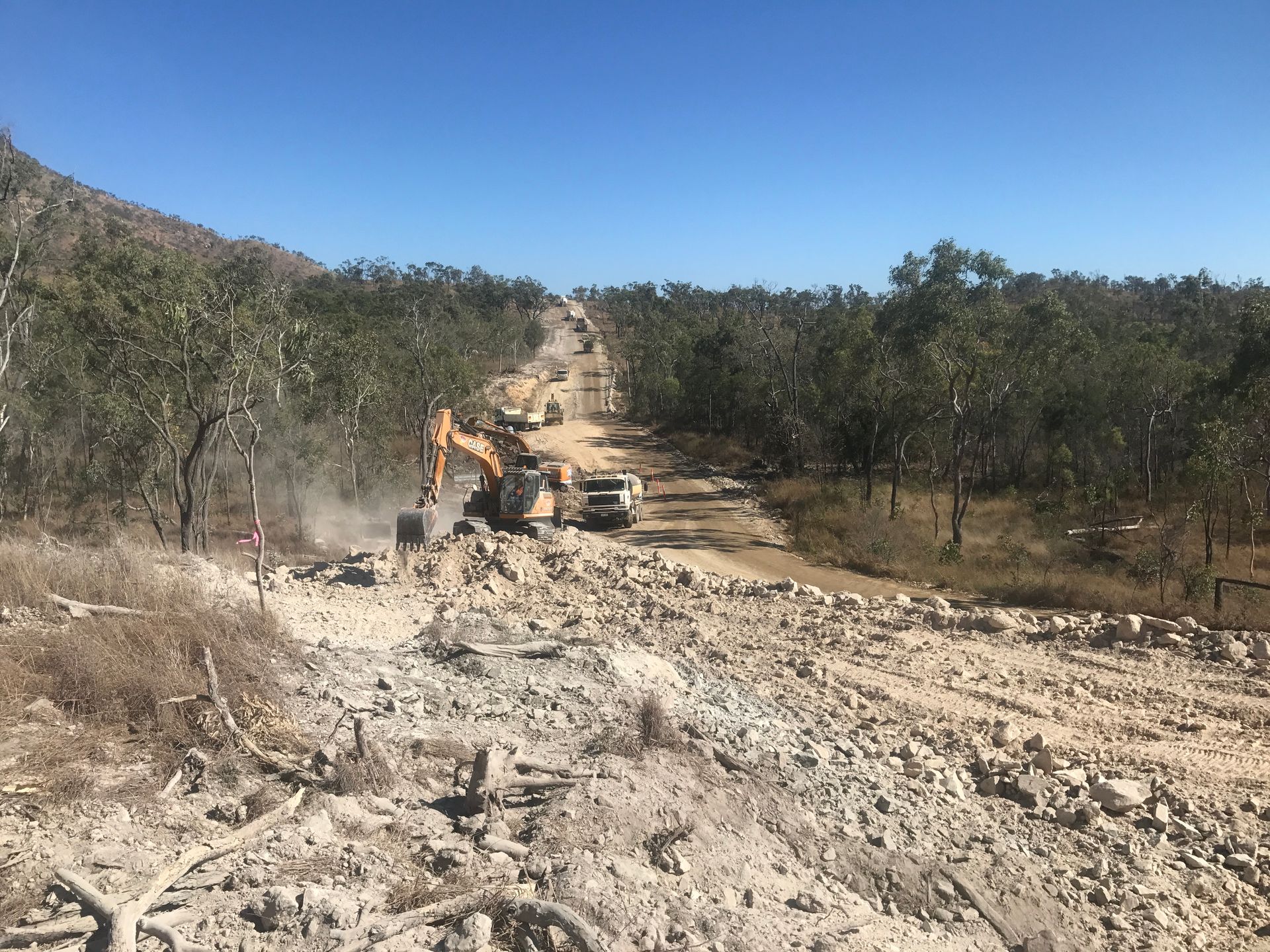 A Dump Truck Is Driving Down a Dirt Road Next to An Excavator — Watto's Earthmoving & Machinery Hire in Atherton, QLD