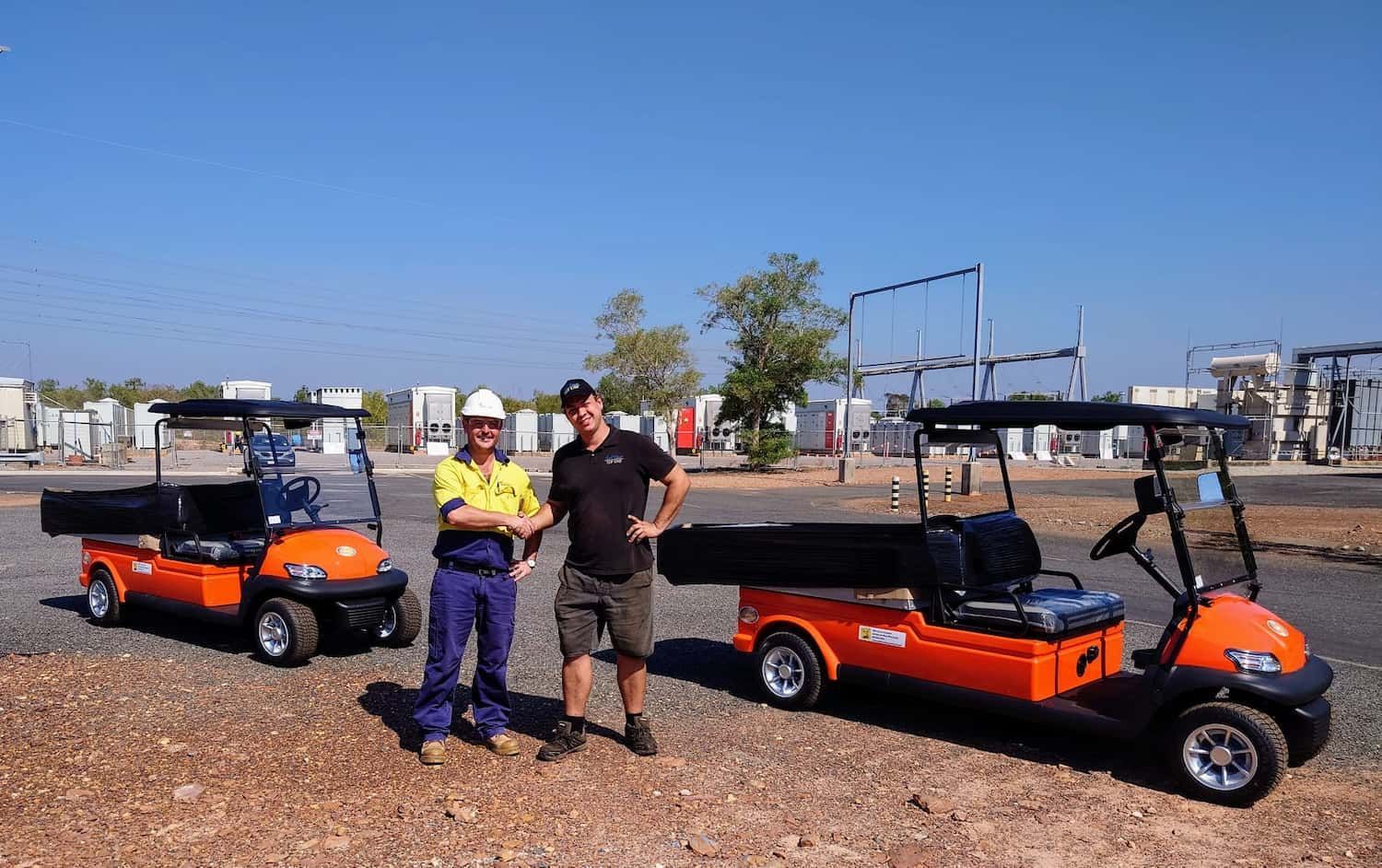 Two Men Are Standing in Front of Two Orange Golf Carts — Golf Carts Top End in Darwin, NT