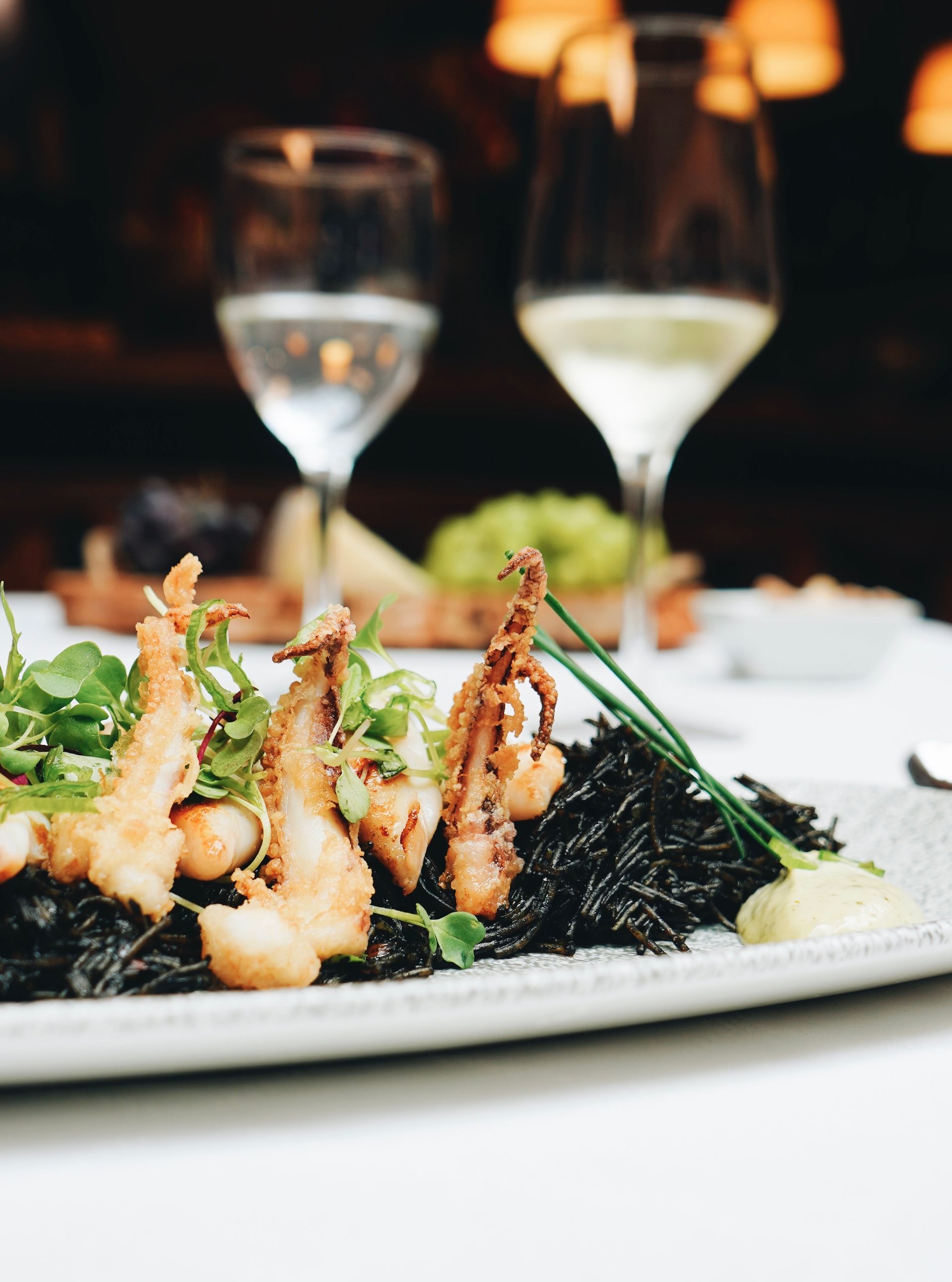 Un plato de comida con una copa de vino al fondo.