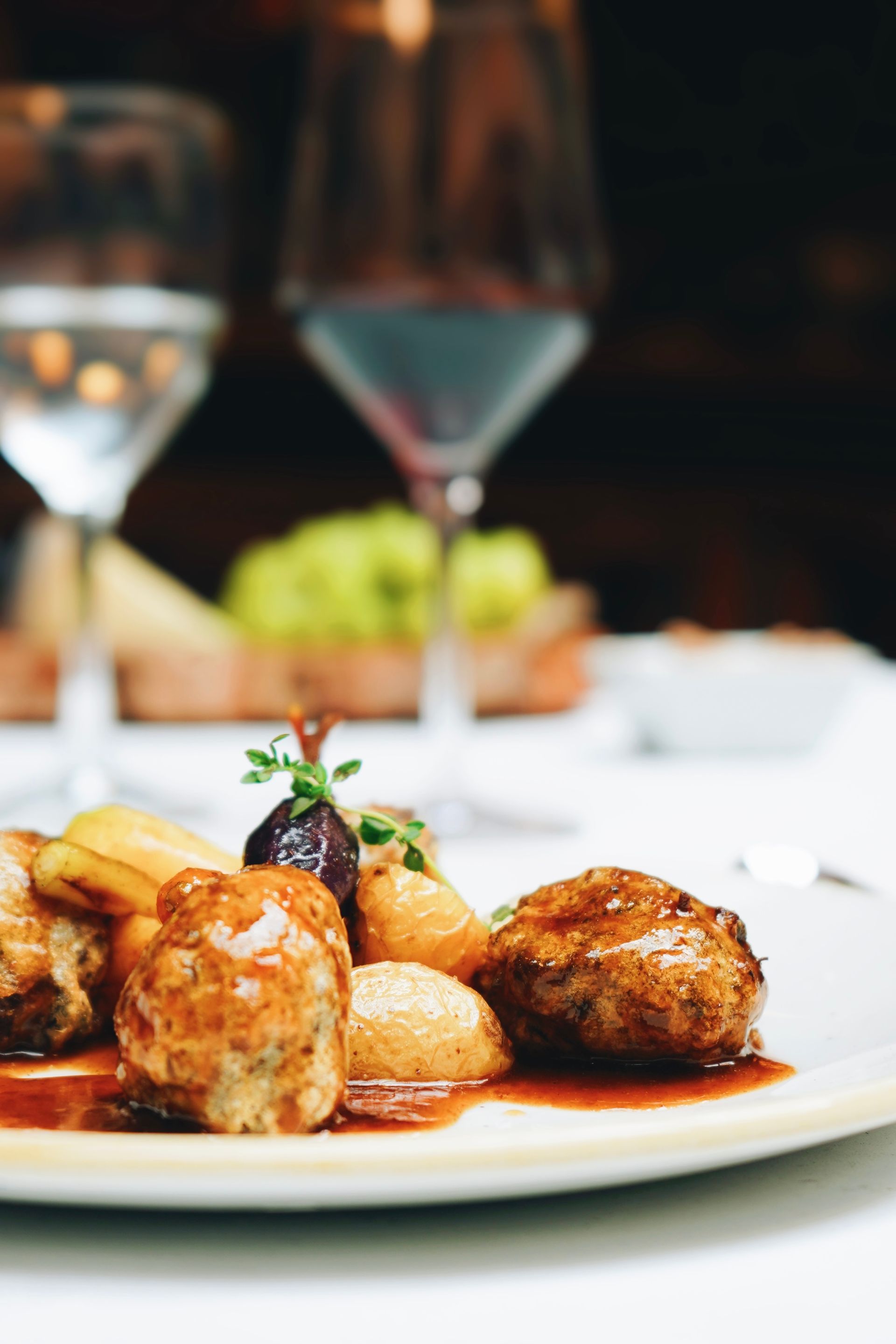 Un primer plano de un plato de comida con una copa de vino al fondo.