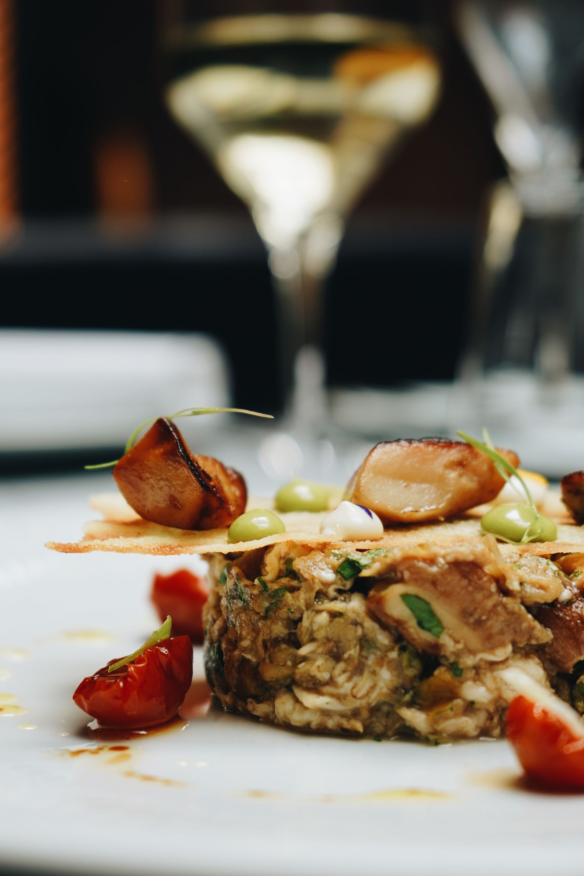 Un primer plano de un plato de comida con una copa de vino al fondo.