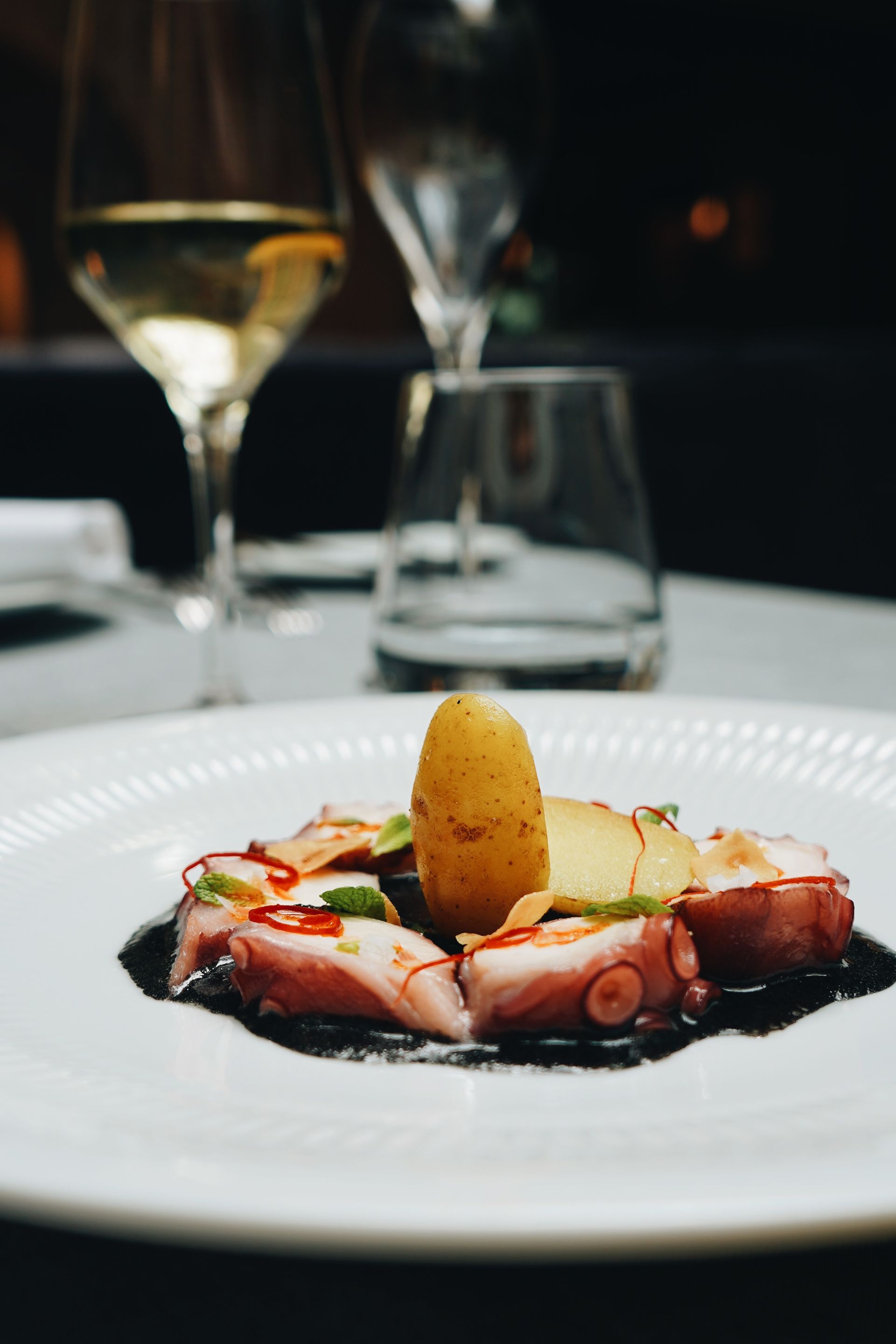 Un plato de comida con una copa de vino al fondo.