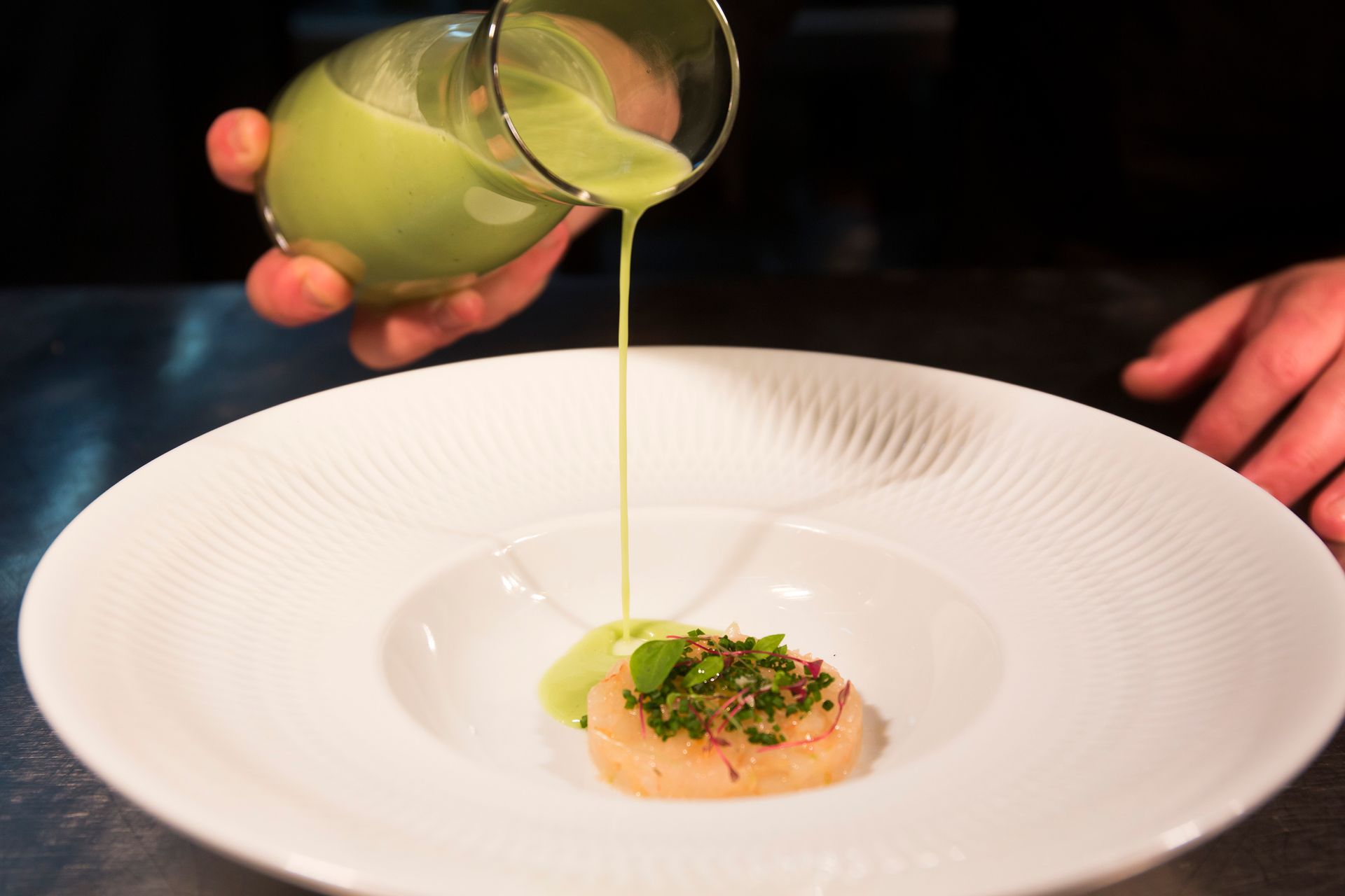 Una persona vertiendo un líquido verde en un plato de comida.