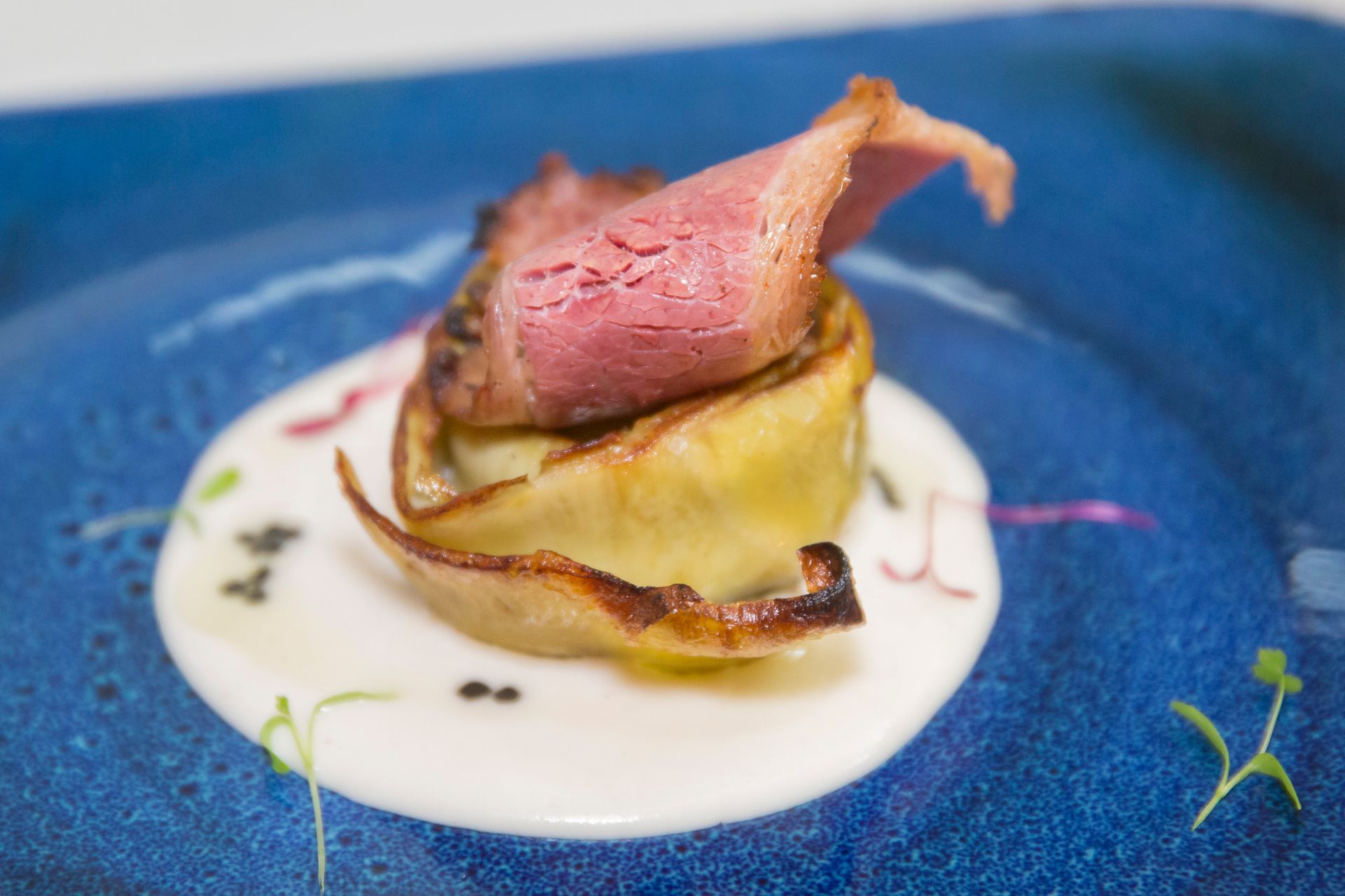 Un plato azul rematado con un trozo de carne y salsa blanca.