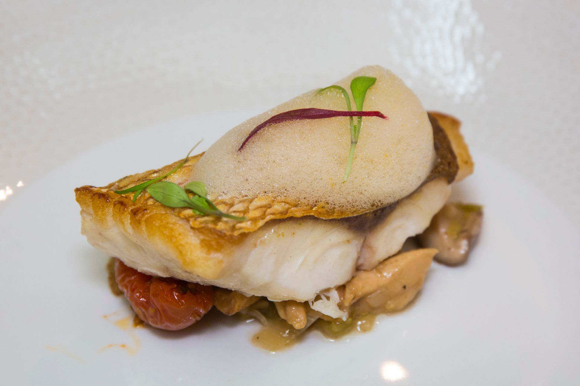Un plato blanco rematado con un trozo de pescado y verduras.
