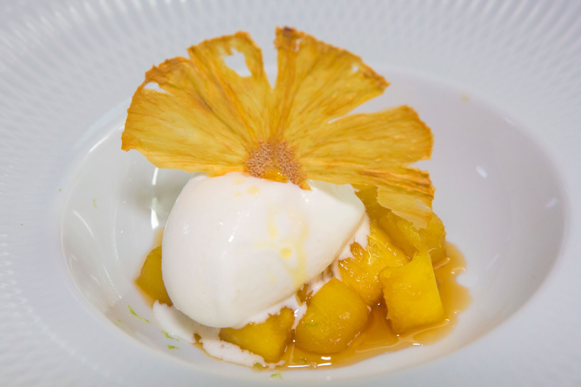 Un plato blanco rematado con una bola de helado y rodajas de piña.