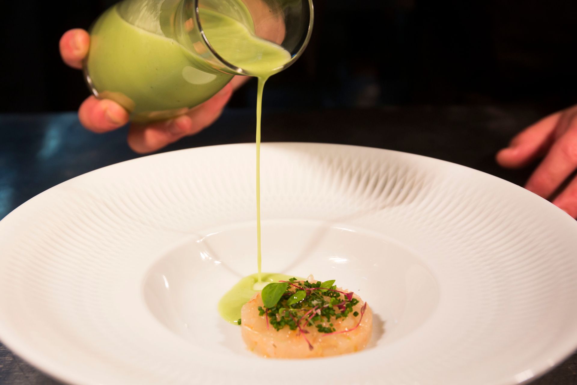 Una persona está echando salsa verde en un plato de comida.