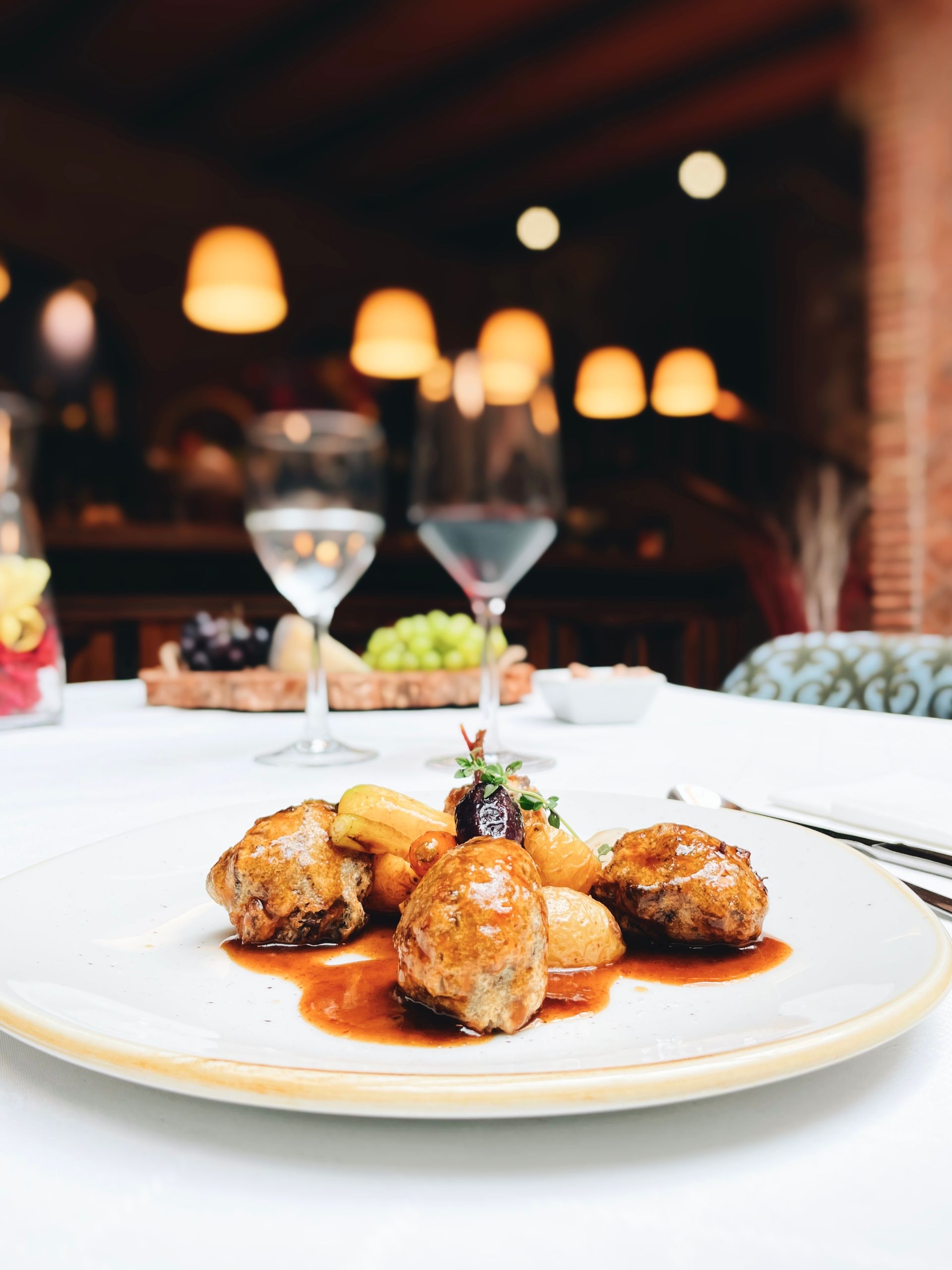 Un plato de comida sobre una mesa con copas de vino al fondo