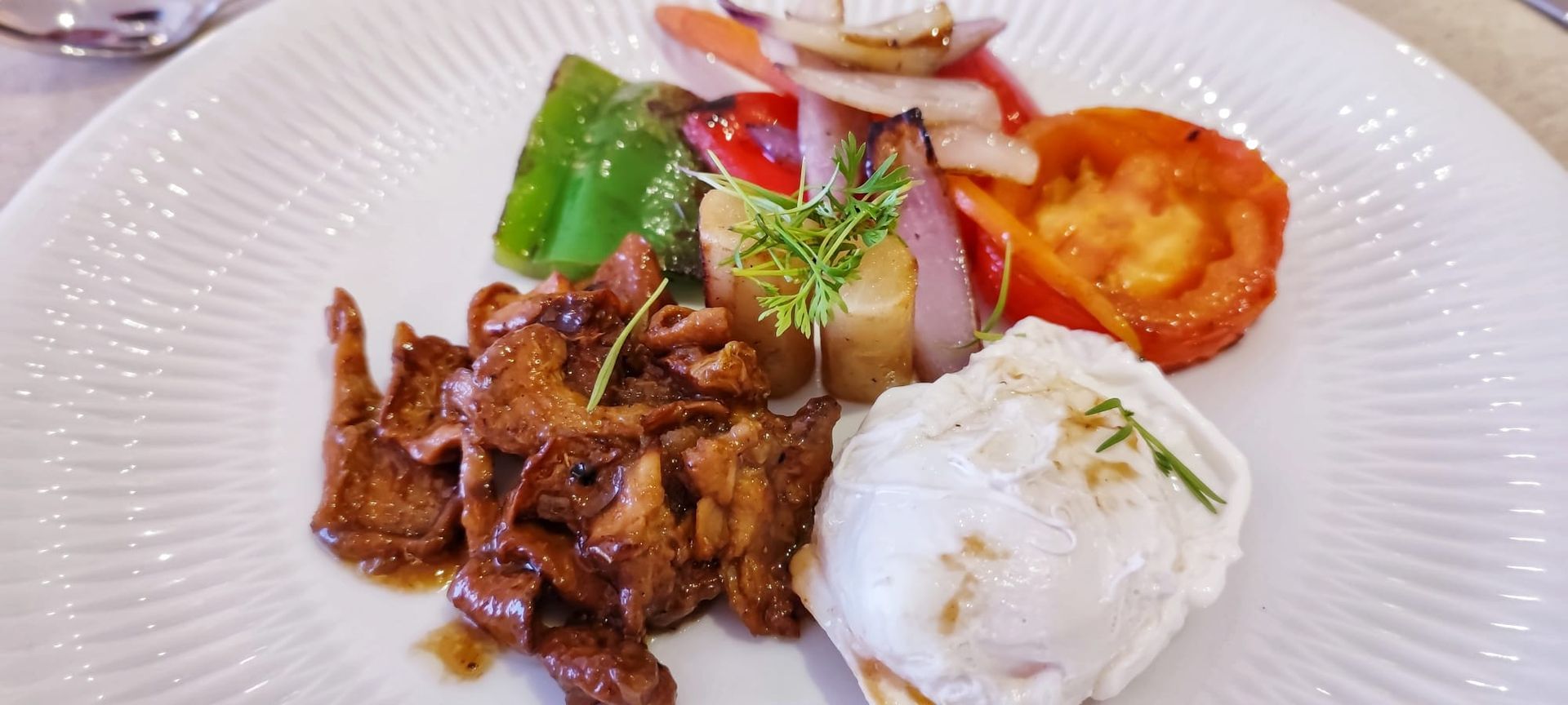 Un plato blanco cubierto con carne, verduras y un huevo escalfado.