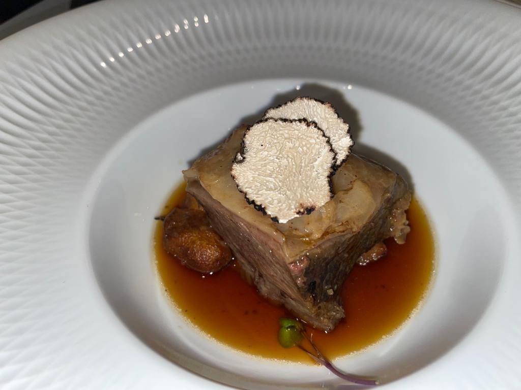Un plato blanco rematado con un trozo de carne y un trozo de trufa.