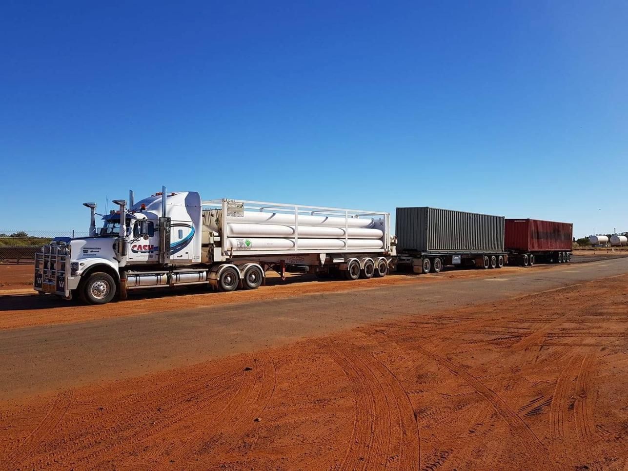 A Semi Truck Is Driving Down a Dirt Road Next to A Train — Spinifex Container Solutions In Ciccone, NT