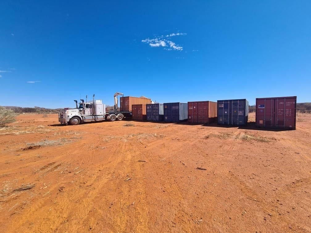 A Truck Is Driving Down a Dirt Road Next to A Row of Shipping Containers — Spinifex Container Solutions In Ciccone, NT